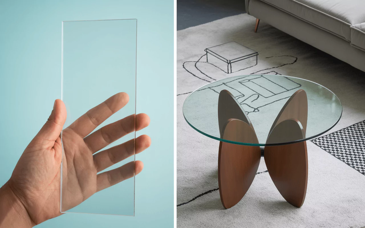 Hand holding a clear acrylic sheet and a round glass table with wooden butterfly base on a rug.