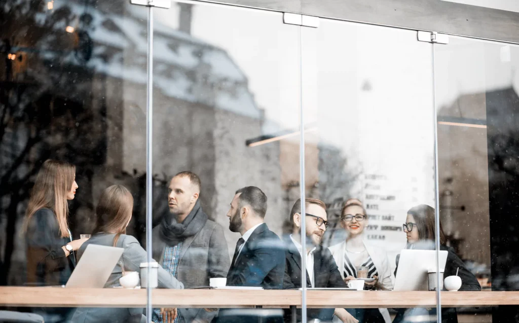 Group of people having a meeting in a café or office behind large clear glass window panels.