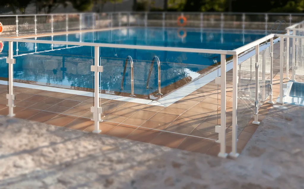  Modern glass railing installed around an outdoor swimming pool with metal frame supports.