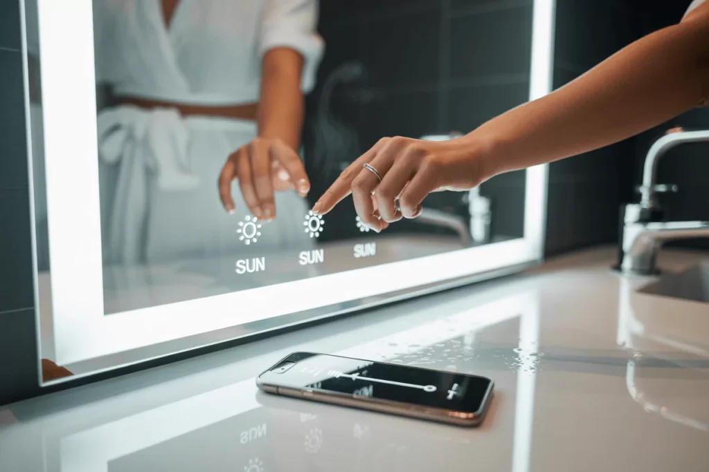 Modern bath with glowing LED mirror; person taps touch controls; anti-fog area clear in steam; phone shows dimmer.