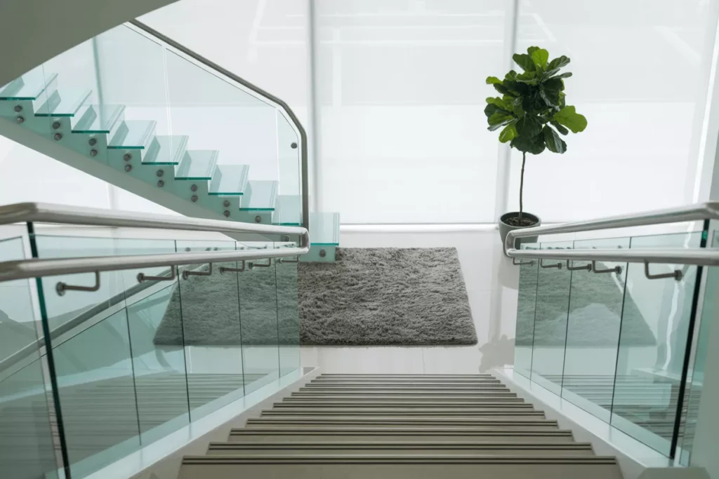 Modern staircase and balcony with tempered glass railings secured by stainless steel clamps in a sleek design.