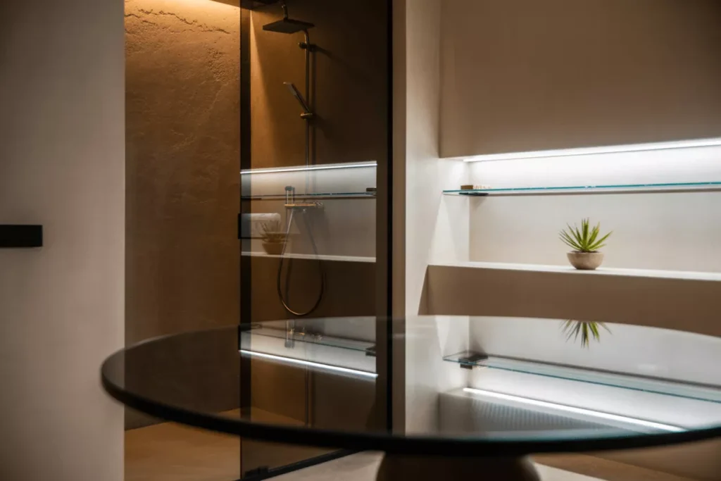 Custom tempered glass in a modern home: frameless shower, rounded glass table, and floating shelves with sleek edges.