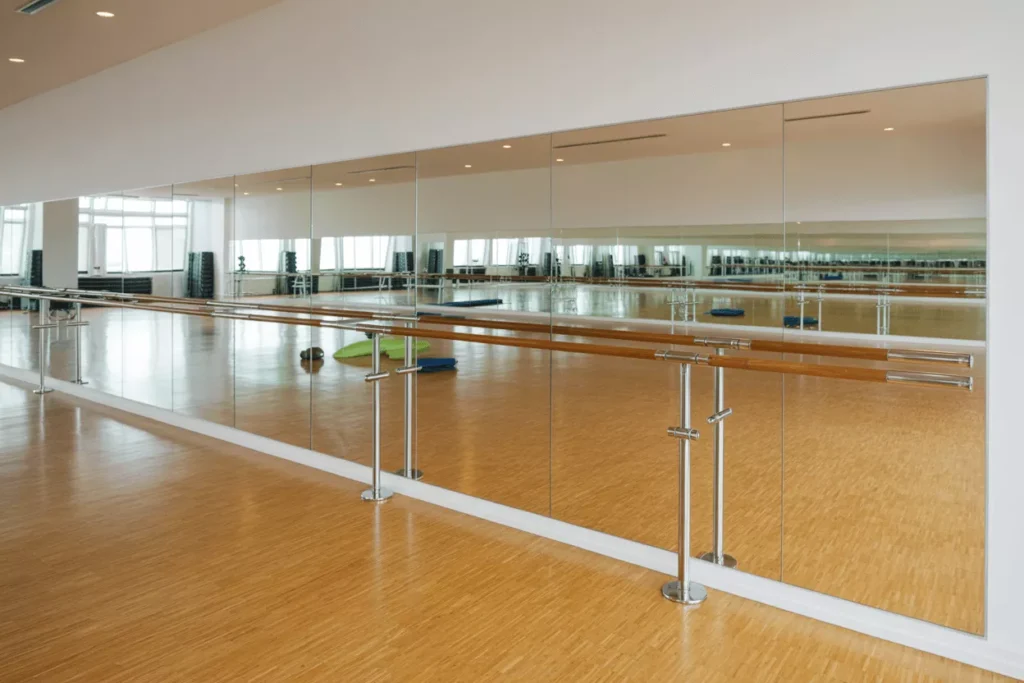 Large glassless mirrors in a bright gym reflecting clear images, offering lightweight, shatterproof safety for active spaces.