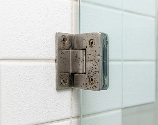Rusty and corroded old glass shower door hinge mounted on white tiled wall