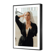 Woman looking into a framed mirror, wearing a black robe in a well-lit room.