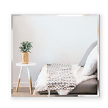 Square mirror above a comfy sofa with a throw blanket and plant.
