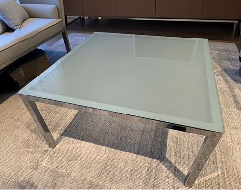 Sleek frosted glass coffee table with chrome legs on a textured rug