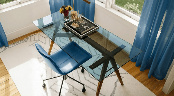 Modern glass desk with blue tempered glass top and matching blue office chair by the window.