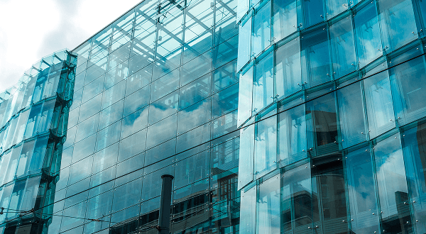 Contemporary building facade featuring large panels of reflective blue tempered glass.