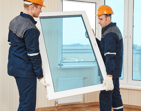 Two workers carefully installing a window frame with blue tempered glass.