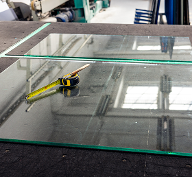 Large glass panels on a workshop table with a tape measure on top.