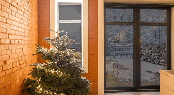 Festive Christmas tree with lights beside a window with ECL tinted grey glass in a cozy brick room.