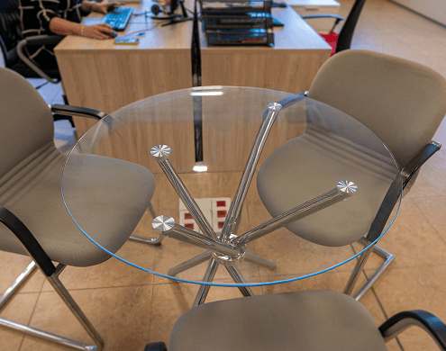 Round glass top for office desk mounted on chrome spider base in open office workspace