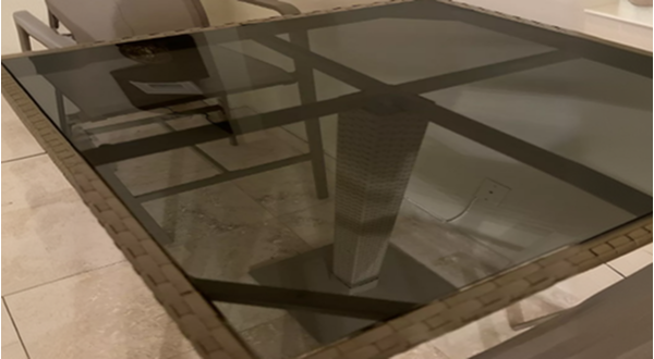 Stylish outdoor dining table with dark light grey glass top and woven rattan base