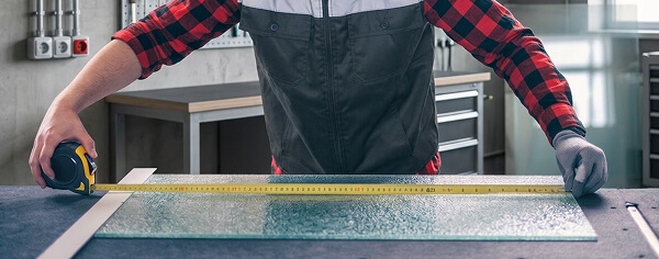 Worker measuring a large sheet of Spraylite tempered glass cut to size on a workbench
